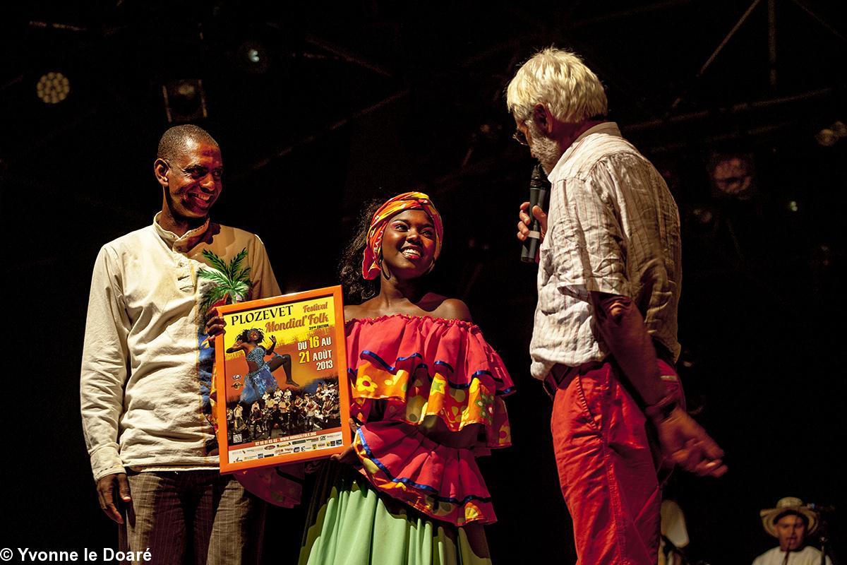 Pierrôt Bosser, Ex-Président du Mondial  Folk, (pendant 25 ans) , remercie la jeune fille Kissi, du groupe de Colombie représentée sur l'affiche  en la lui offrant encadrée.