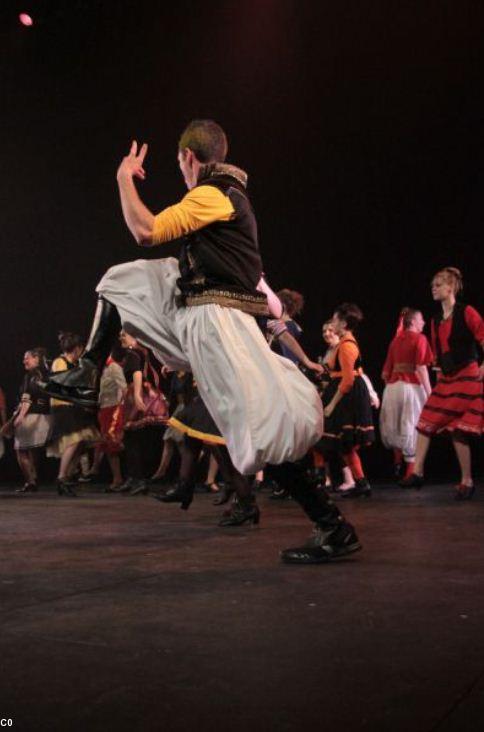 la photo représente, au premier plan,le saut dans la danse d'un danseur en costume, et plus loin d'autres danseurs.